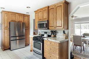 Kitchen featuring stainless steel appliances, a ceiling fan, wood cabinets, and light granite countertops