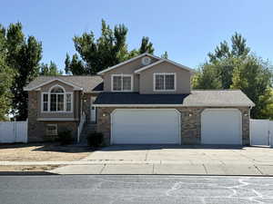 Tri-level home featuring driveway, a gate, roof with shingles, and an attached garage