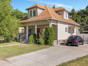View of front of house featuring covered porch, a shingled roof, and a front lawn