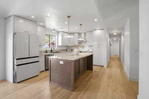 Kitchen featuring freestanding refrigerator, stainless steel dishwasher, recessed lighting, a center island, and light wood-type flooring
