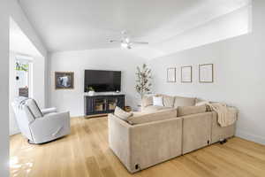 Living room with vaulted ceiling, a ceiling fan, and light wood finished floors