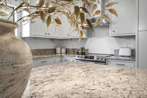 Kitchen featuring stainless steel electric range, light stone countertops, and white cabinets