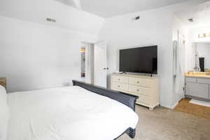 Bedroom with light carpet, ensuite bath, light tile patterned flooring, and lofted ceiling