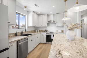 Kitchen with appliances with stainless steel finishes, wall chimney exhaust hood, light wood-style floors, white cabinets, and recessed lighting