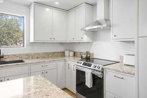Kitchen featuring wall chimney exhaust hood, stainless steel electric range, white cabinets, and recessed lighting