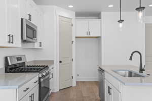 Kitchen featuring stainless steel appliances, light wood finished floors, recessed lighting, pendant lighting, and white cabinetry