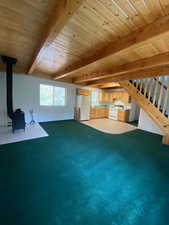 Unfurnished living room with a wood stove, a wooden ceiling with exposed beams, carpet floors, and stairs