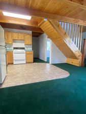 Kitchen featuring light brown cabinetry, white appliances, a wooden ceiling with exposed beams, light countertops, and light colored carpet