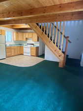 Kitchen featuring light brown cabinetry, white appliances, a wooden ceiling with exposed beams, light countertops, and carpet floors
