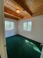 Spare room with a wooden ceiling with exposed beams and dark carpet