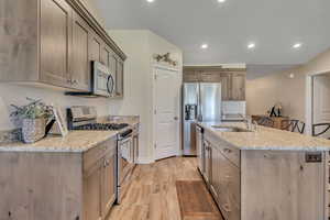Kitchen featuring stainless steel appliances, light wood finished floors, an island with sink, recessed lighting, and light stone countertops
