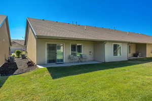 Back of property with stucco siding, a patio area, a lawn, and a shingled roof