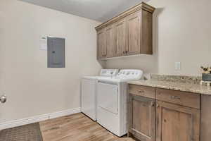Washroom featuring electric panel, cabinet space, washer and clothes dryer, light wood-style flooring, and a textured ceiling