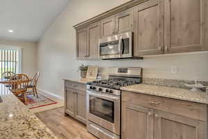 Kitchen featuring appliances with stainless steel finishes, light wood-style floors, light stone countertops, recessed lighting, and vaulted ceiling