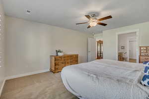 Bedroom with light carpet, ceiling fan, and ensuite bath
