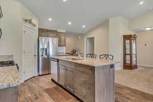 Kitchen featuring appliances with stainless steel finishes, light wood-style flooring, recessed lighting, light stone counters, and an island with sink