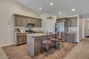 Kitchen featuring stainless steel appliances, lofted ceiling, light wood-style floors, a breakfast bar, and a center island with sink