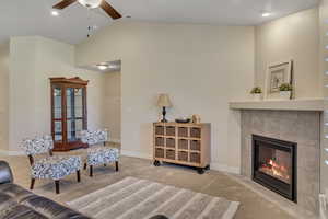Living room featuring carpet flooring, lofted ceiling, a ceiling fan, and a fireplace