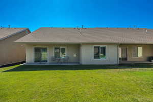 Rear view of property with stucco siding, a patio, a lawn, and a shingled roof