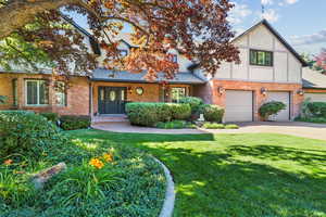 English style home with concrete driveway, a front yard, an attached garage, and brick siding