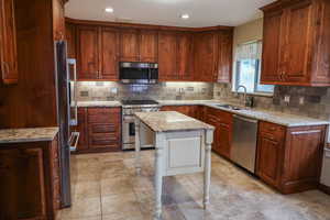 Kitchen featuring light stone countertops, premium appliances, backsplash, a breakfast bar area, and recessed lighting