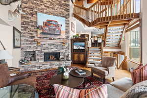 Living area featuring wood finished floors, a towering ceiling, stairs, and a stone fireplace
