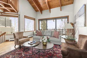 Living area with a baseboard radiator, a wood ceiling with exposed beams, wood finished floors, and high vaulted ceiling