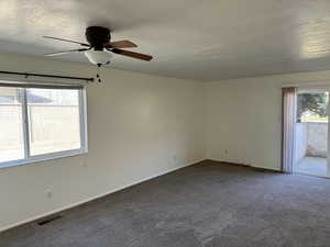 Unfurnished room with dark carpet, a textured ceiling, and ceiling fan