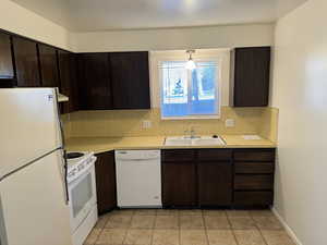 Kitchen with dark brown cabinets, white appliances, light countertops, decorative light fixtures, and backsplash