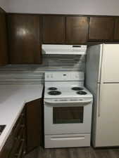 Kitchen with dark brown cabinets, white appliances, light countertops, and under cabinet range hood