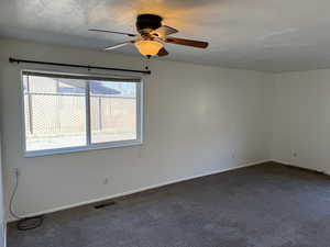 Empty room featuring dark carpet, a textured ceiling, and a ceiling fan
