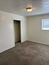 Unfurnished bedroom with a textured ceiling, dark colored carpet, and a closet