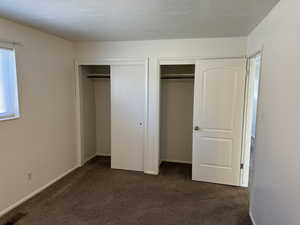 Unfurnished bedroom with two closets and dark colored carpet