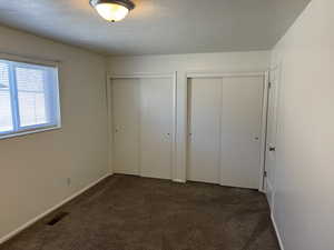 Unfurnished bedroom with two closets, dark colored carpet, and a textured ceiling