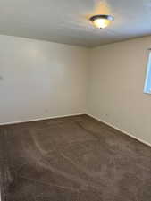 Empty room with dark carpet and a textured ceiling