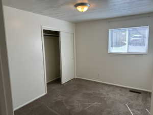 Unfurnished bedroom with dark carpet, a closet, and a textured ceiling