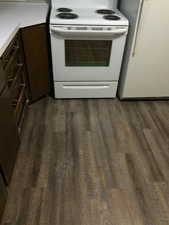 Kitchen view of white appliances, dark brown cabinets, dark wood-style floors, and light countertops