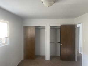 Unfurnished bedroom with two closets, carpet, and a textured ceiling