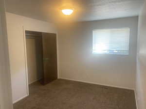 Unfurnished bedroom featuring dark colored carpet, a closet, and a textured ceiling
