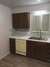 Kitchen featuring dark brown cabinetry, light countertops, white dishwasher, and backsplash
