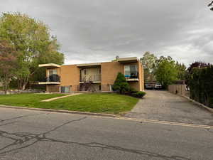 View of front of property with a front lawn, stucco siding, a balcony, and driveway