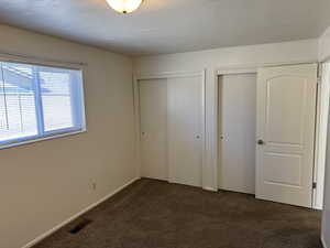 Unfurnished bedroom with two closets, dark carpet, and a textured ceiling