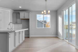 Kitchen with decorative backsplash, a chandelier, light stone countertops, pendant lighting, and light wood-style flooring