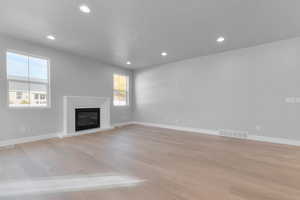 Unfurnished living room featuring light wood-style floors, recessed lighting, and a glass covered fireplace