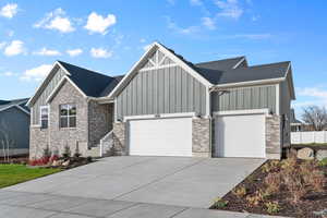 View of front of property with board and batten siding, concrete driveway, a garage, brick siding, and a shingled roof