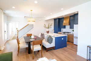 Kitchen with high end stainless steel range, custom exhaust hood, freestanding refrigerator, blue cabinets, and light wood-style floors