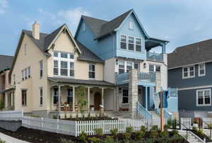 View of front facade with covered porch, stucco siding, a chimney, a fenced front yard, and roof with shingles