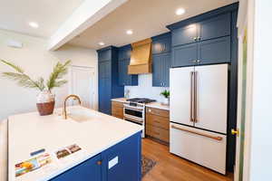 Kitchen with premium appliances, blue cabinetry, premium range hood, light wood finished floors, and recessed lighting