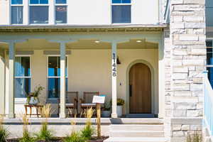 Entrance to property with stucco siding, stone siding, and covered porch
