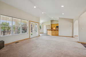 Unfurnished living room featuring vaulted ceiling, light colored carpet, arched walkways, recessed lighting, and french doors